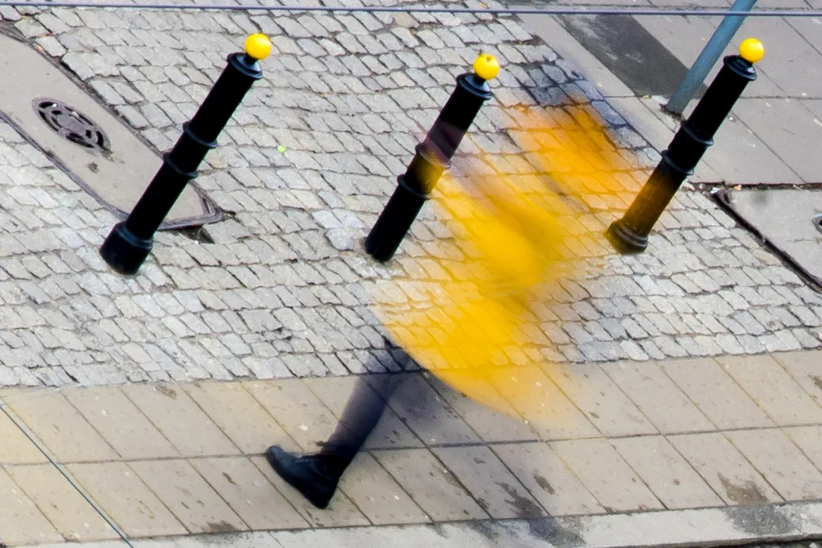 Yellow-coated figure blurred between black bollards